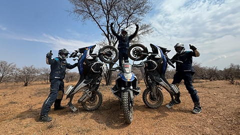 L’équipe masculine du Benelux interprète sa pyramide avec un pilote debout au centre sur sa moto, les mains en l’air, tandis que les deux autres pilotes ont placé leur moto sur la roue arrière et tiennent le pouce vers le haut.