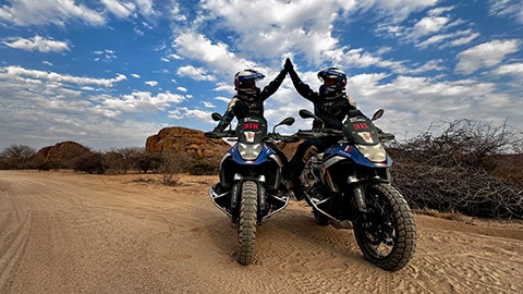 Deux pilotes de l’équipe féminine de France sont assises sur leur moto BMW R 1300 GS Competition et se tapent dans la main.