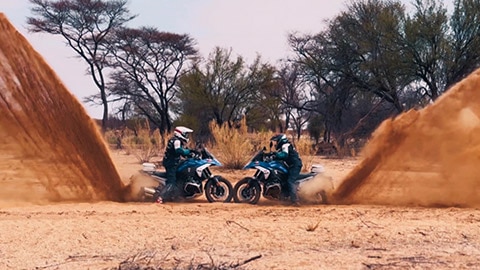 Deux pilotes de l’équipe internationale présentent leur roue avant face à face en chassant une grande quantité de sable avec leur roue arrière.