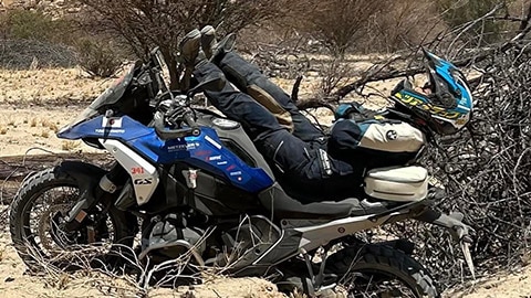 Une pilote de l’équipe féminine du Japon est allongée sur sa BMW R 1300 GS. Ses jambes sont tendues vers le guidon tandis que ses épaules et sa tête dépassent de l’arrière de la moto.